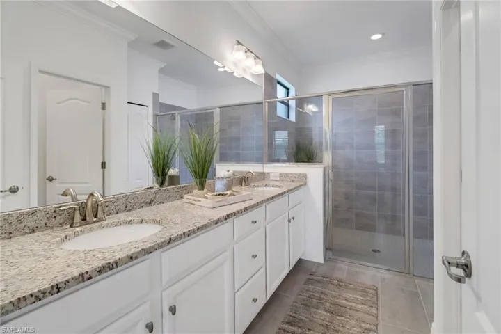 Bathroom featuring a shower with shower door, crown molding, tile patterned floors, and double sink vanity