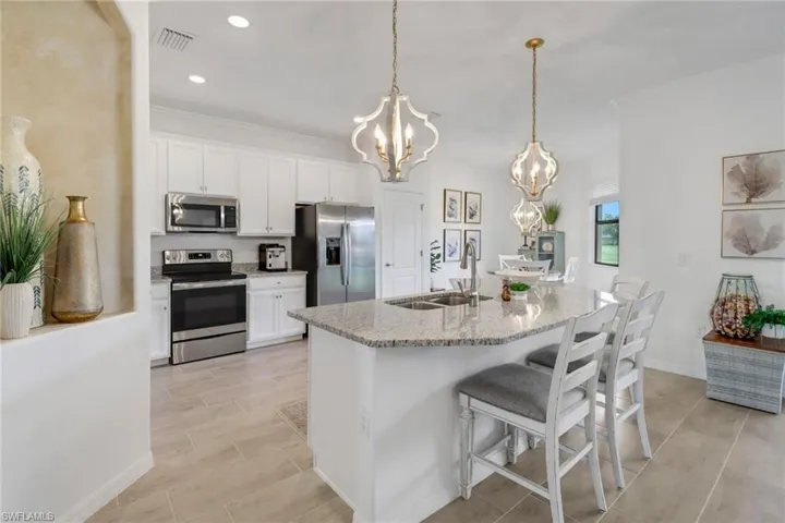 Kitchen featuring white cabinets, stainless steel appliances, light stone countertops, and hanging light fixtures
