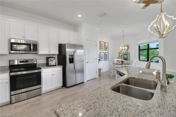 Kitchen featuring sink, light stone countertops, stainless steel appliances, and white cabinetry