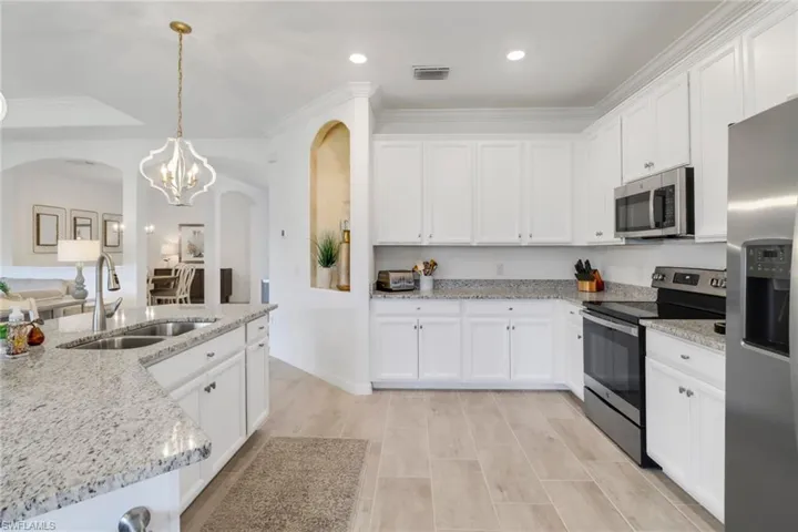 Kitchen with white cabinetry, crown molding, stainless steel appliances, light stone countertops, and sink