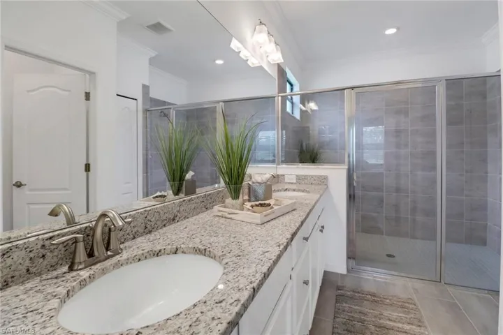 Bathroom featuring an enclosed shower, crown molding, tile patterned floors, and double sink vanity