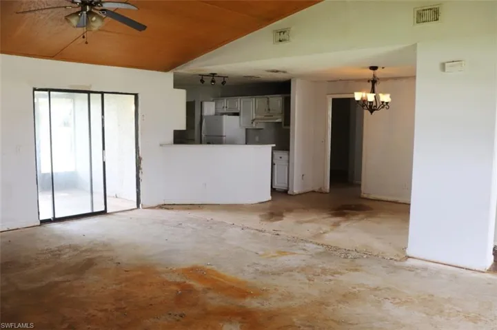 Unfurnished living room with ceiling fan with notable chandelier, vaulted ceiling, and wood ceiling