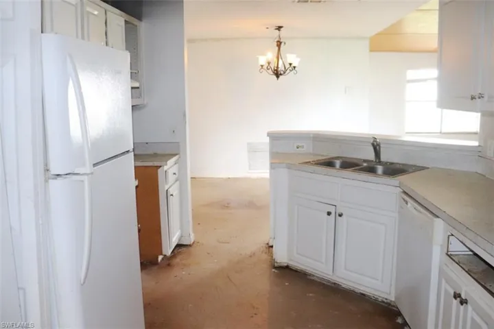 Kitchen featuring white cabinets, pendant lighting, sink, white appliances, and an inviting chandelier