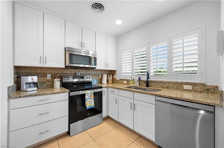 Kitchen with light stone countertops, white cabinetry, stainless steel appliances, light tile patterned floors, and recessed lighting