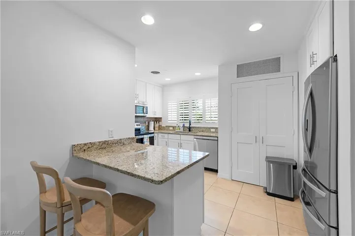 Kitchen featuring light stone counters, a peninsula, a kitchen bar, stainless steel appliances, and white cabinets
