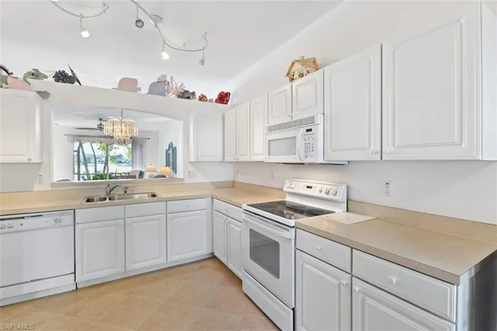 Kitchen featuring white appliances, track lighting, light tile floors, sink, and white cabinetry