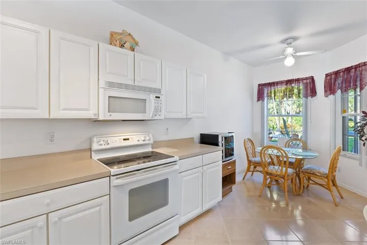 Kitchen with white cabinets, ceiling fan, white appliances, and light tile floors