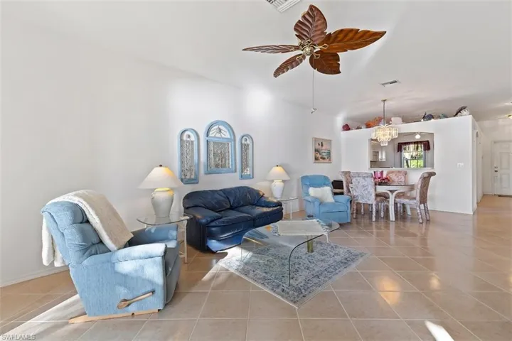 Tiled living room with ceiling fan with notable chandelier