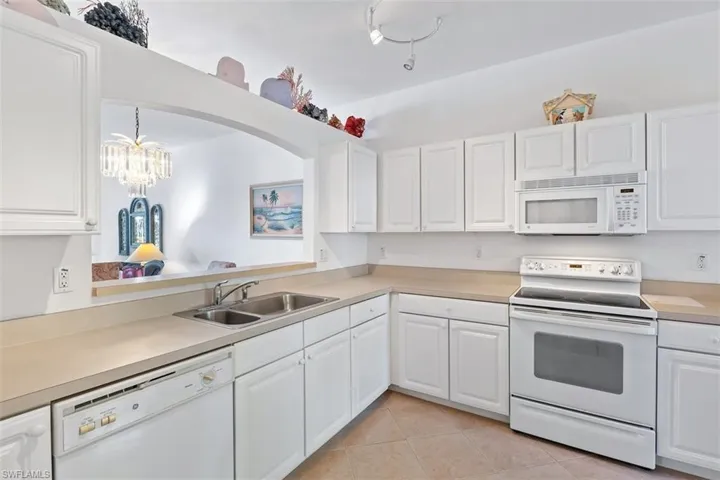 Kitchen with a chandelier, white cabinetry, sink, white appliances, and light tile floors