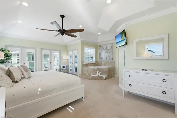 Tray ceiling featuring recessed lighting and a ceiling fan, multiple French doors with plantation shutters, built-in jetted tub with stone-look surround, and plush carpeting - Virtually Edited Image