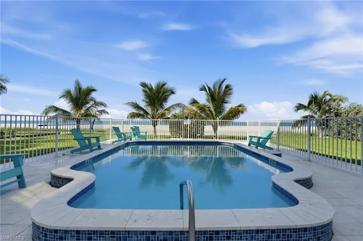 Fenced in-ground pool with integrated steps, surrounded by a paved patio and manicured lawn  - Virtually Edited Image