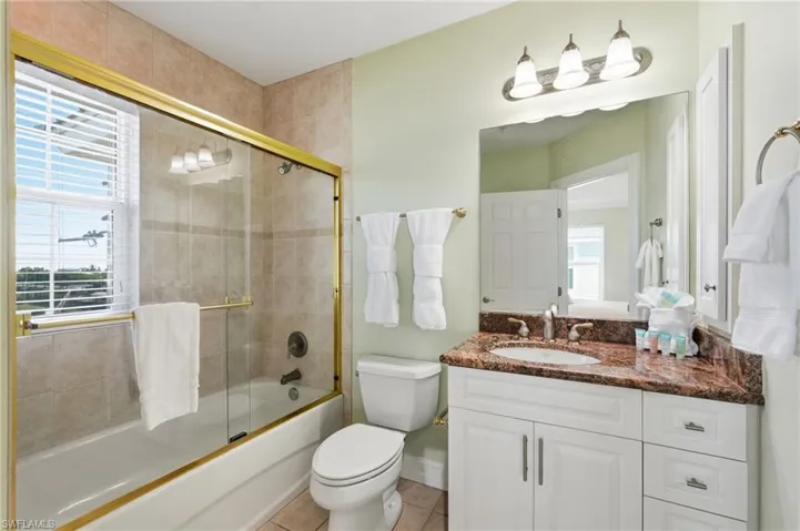 Bathroom featuring a vanity with a dark marble-finish countertop, single basin sink, and white cabinetry - Virtually Edited Image