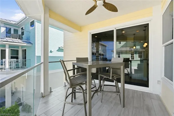 Covered balcony with wood-finish flooring, glass panel railing, and a ceiling fan - Virtually Edited Image
