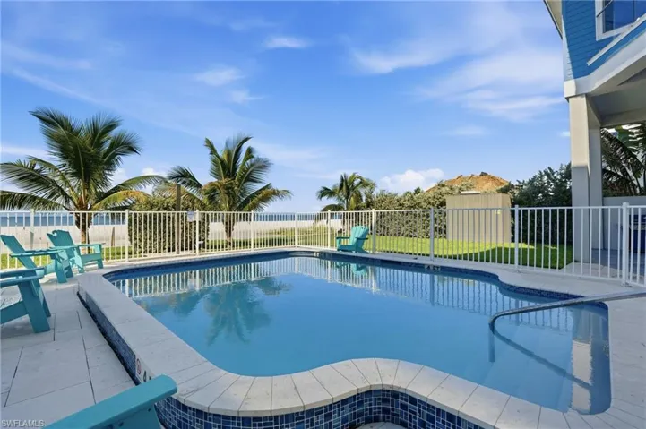 Resort-style pool with mosaic tile accents, surrounded by a paved patio and white fencing - Virtually Edited Image