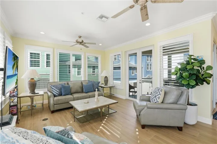 Expansive open-concept interior featuring light wood-finish flooring, white plantation shutters, and a ceiling fan with integrated lighting - Virtually Edited Image