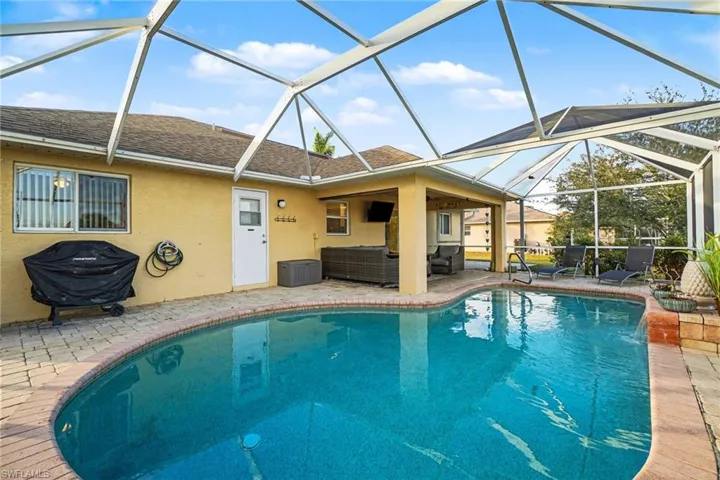 Screened-in outdoor living space featuring a free-form swimming pool with brick paver surround, covered patio area, and exterior access door