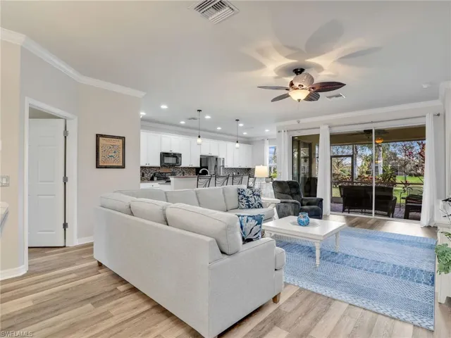 Living room featuring light wood finished floors, baseboards, visible vents, and crown molding