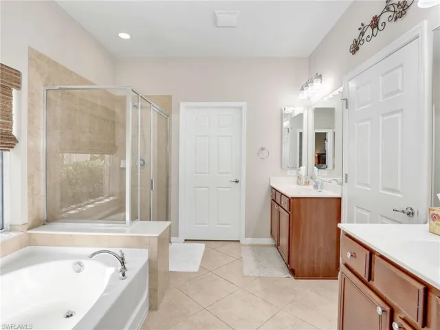 Full bath with two vanities, a sink, a shower stall, tile patterned flooring, and a bath