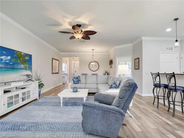 Living area featuring a ceiling fan, baseboards, visible vents, light wood finished floors, and crown molding