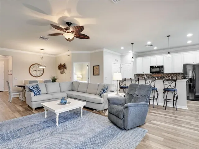 Living area featuring light wood-style flooring, visible vents, and crown molding