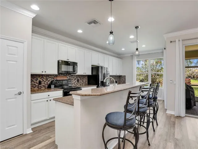Kitchen featuring black appliances, a center island with sink, and crown molding
