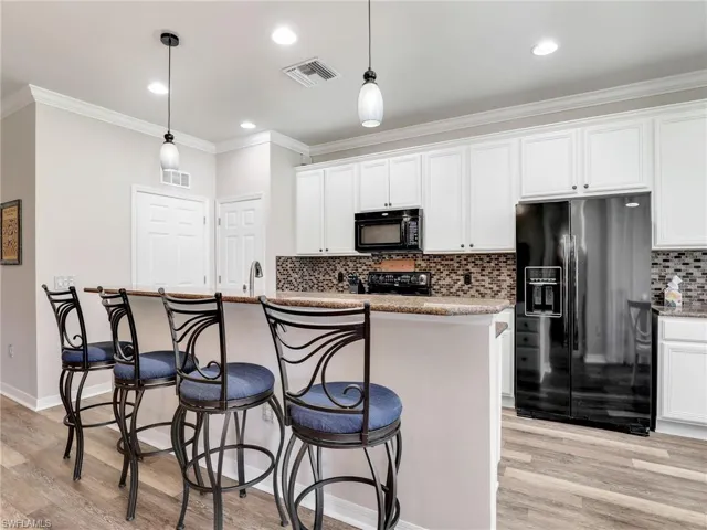 Kitchen with ornamental molding, visible vents, light wood-style flooring, and black appliances