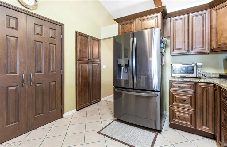 Kitchen with light stone countertops, light tile flooring, stainless steel refrigerator with ice dispenser, and vaulted ceiling
