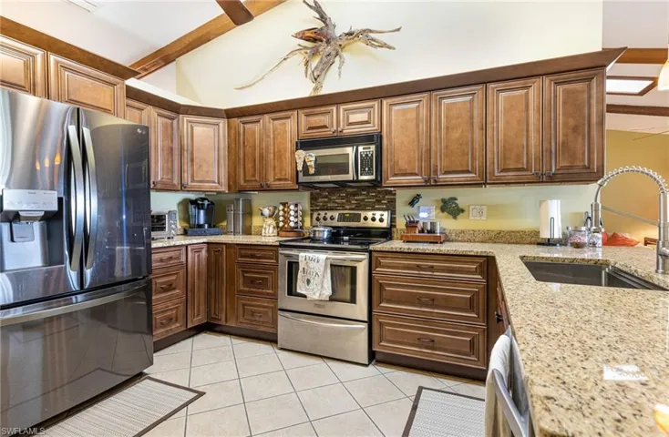 Kitchen with stainless steel appliances, light stone counters, sink, ceiling fan, and light tile floors