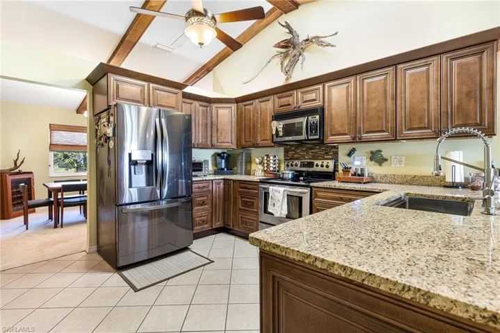 Kitchen featuring tasteful backsplash, stainless steel appliances, vaulted ceiling with beams, light tile floors, and sink