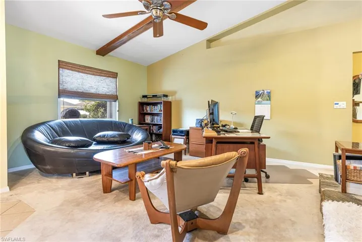 Office area featuring ceiling fan, vaulted ceiling with beams, and light carpet