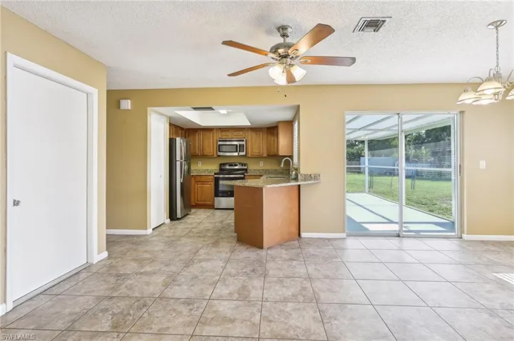 Kitchen featuring light tile flooring, kitchen peninsula, stainless steel appliances, ceiling fan with notable chandelier, and a textured ceiling