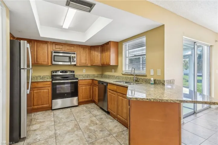 Kitchen featuring plenty of natural light, stainless steel appliances, kitchen peninsula, and light stone countertops