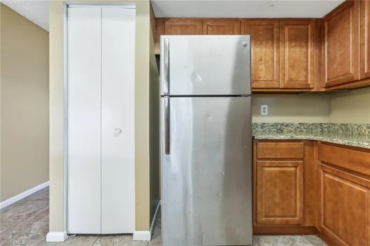 Kitchen featuring light stone countertops, stainless steel refrigerator, and light tile floors