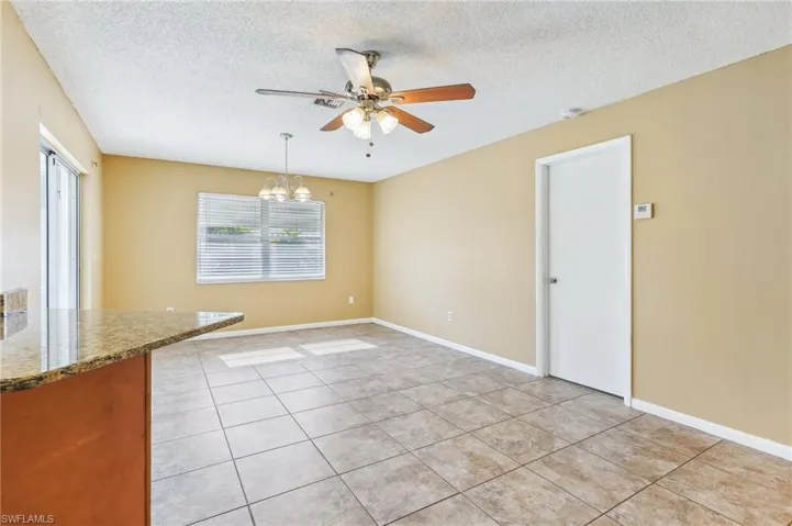 Unfurnished room featuring ceiling fan with notable chandelier, a textured ceiling, and light tile floors