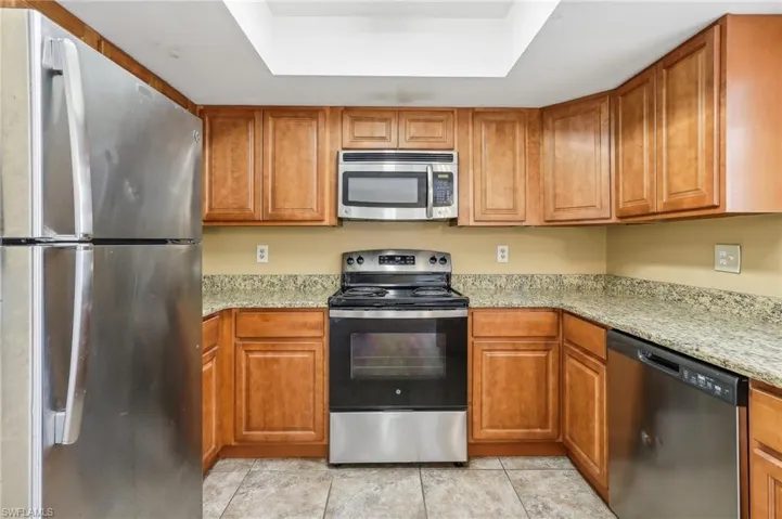Kitchen with stainless steel appliances, light tile floors, a tray ceiling, light stone counters, and a skylight