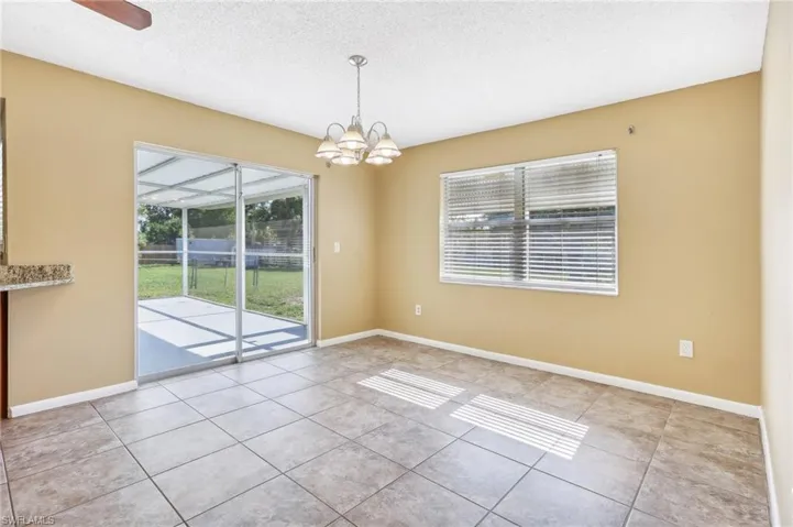 Tiled empty room featuring a textured ceiling and ceiling fan with notable chandelier