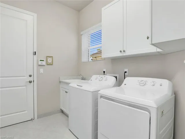 Laundry area with cabinets, light tile flooring, washing machine and clothes dryer, washer hookup, and sink
