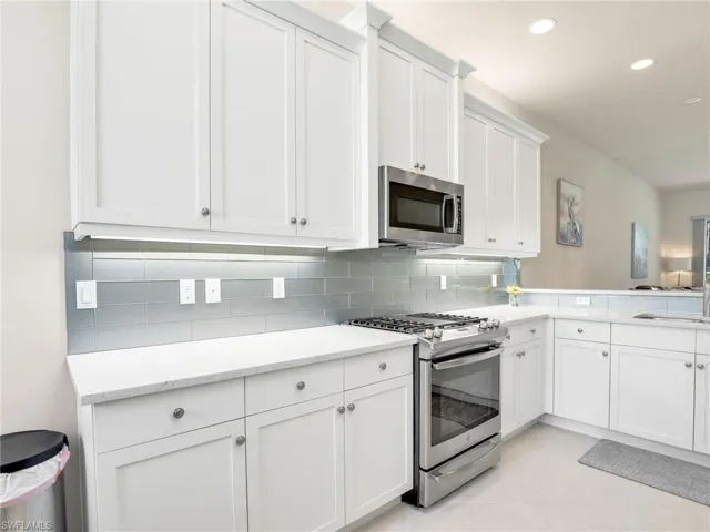 Kitchen featuring light stone counters, backsplash, white cabinetry, appliances with stainless steel finishes, and light tile floors