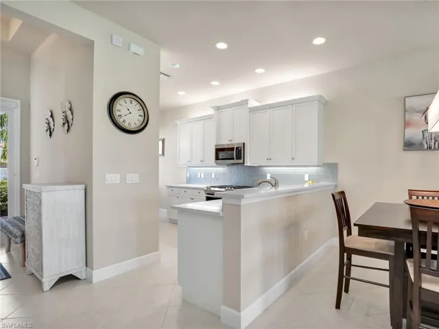Kitchen with kitchen peninsula, tasteful backsplash, stove, light tile floors, and white cabinetry