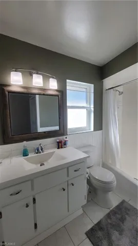 Full bathroom with shower / bath combo with shower curtain, vanity, a wainscoted wall, and light marble finish floors