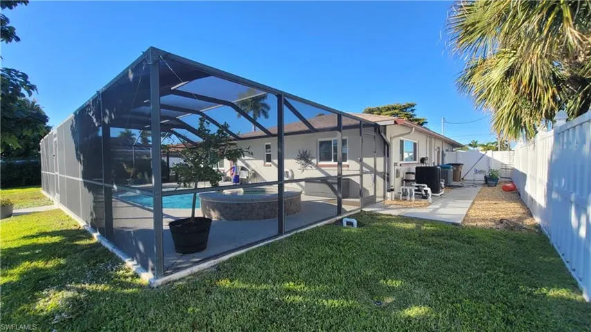 Back of house featuring a sunroom, a lanai, a pool with connected hot tub, a fenced backyard, and a patio