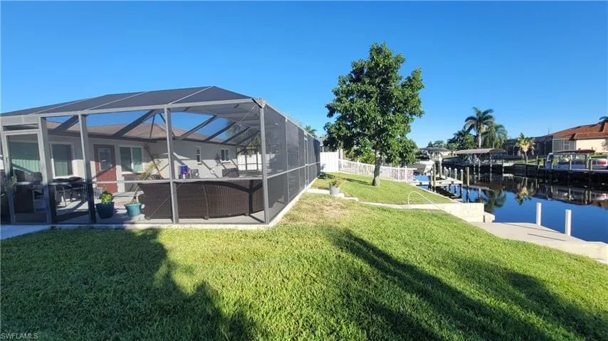 View of grassy yard with a sunroom, glass enclosure, a water view, a dock, and a patio