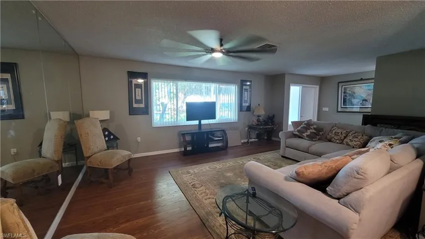 Living area with dark wood-type flooring, a textured ceiling, and ceiling fan