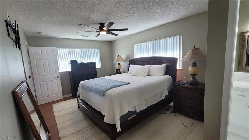 Bedroom with wood finished floors, multiple windows, ceiling fan, and a textured ceiling