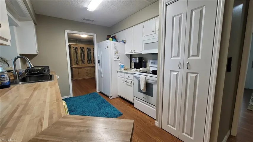Kitchen with white cabinets, white appliances, a textured ceiling, light wood-style floors, and butcher block counters