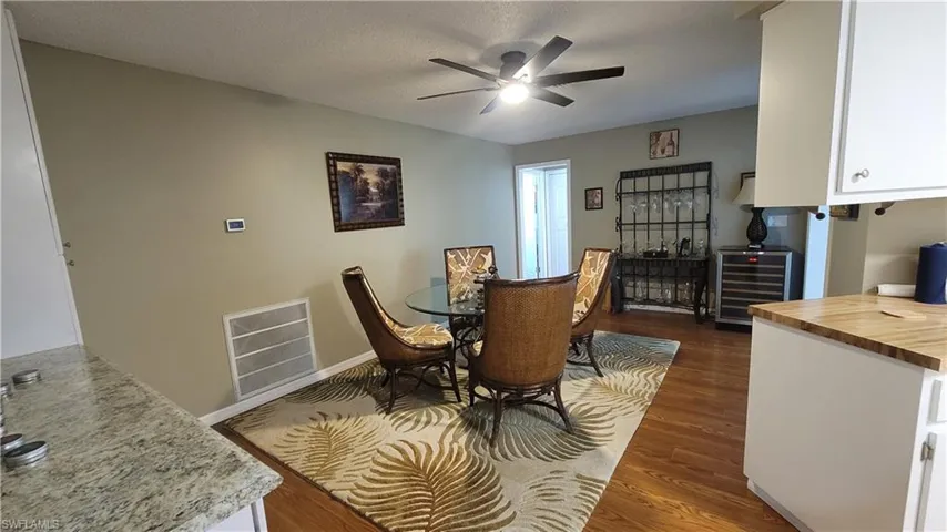 Dining room featuring wine cooler, dark wood-style flooring, a ceiling fan, and a textured ceiling