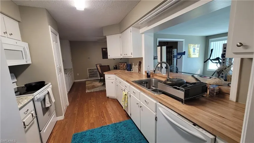Kitchen featuring white appliances, white cabinets, light countertops, a textured ceiling, and dark wood finished floors