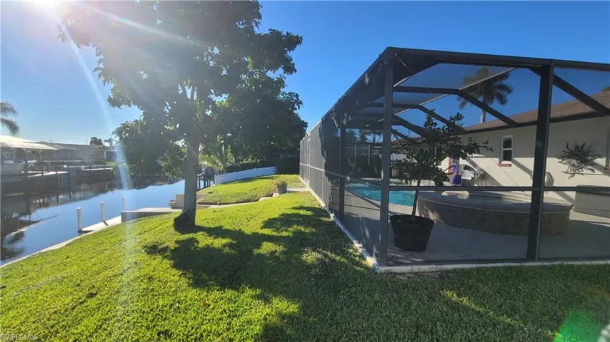 View of yard with a lanai, a sunroom, a water view, and a pool with connected hot tub
