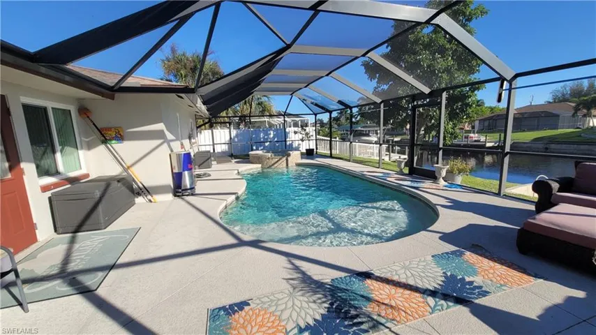 View of swimming pool with glass enclosure, a sunroom, a patio, a pool with connected hot tub, and a water view