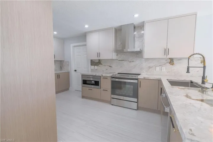 Kitchen featuring appliances with stainless steel finishes, tasteful backsplash, sink, light stone countertops, and wall chimney range hood